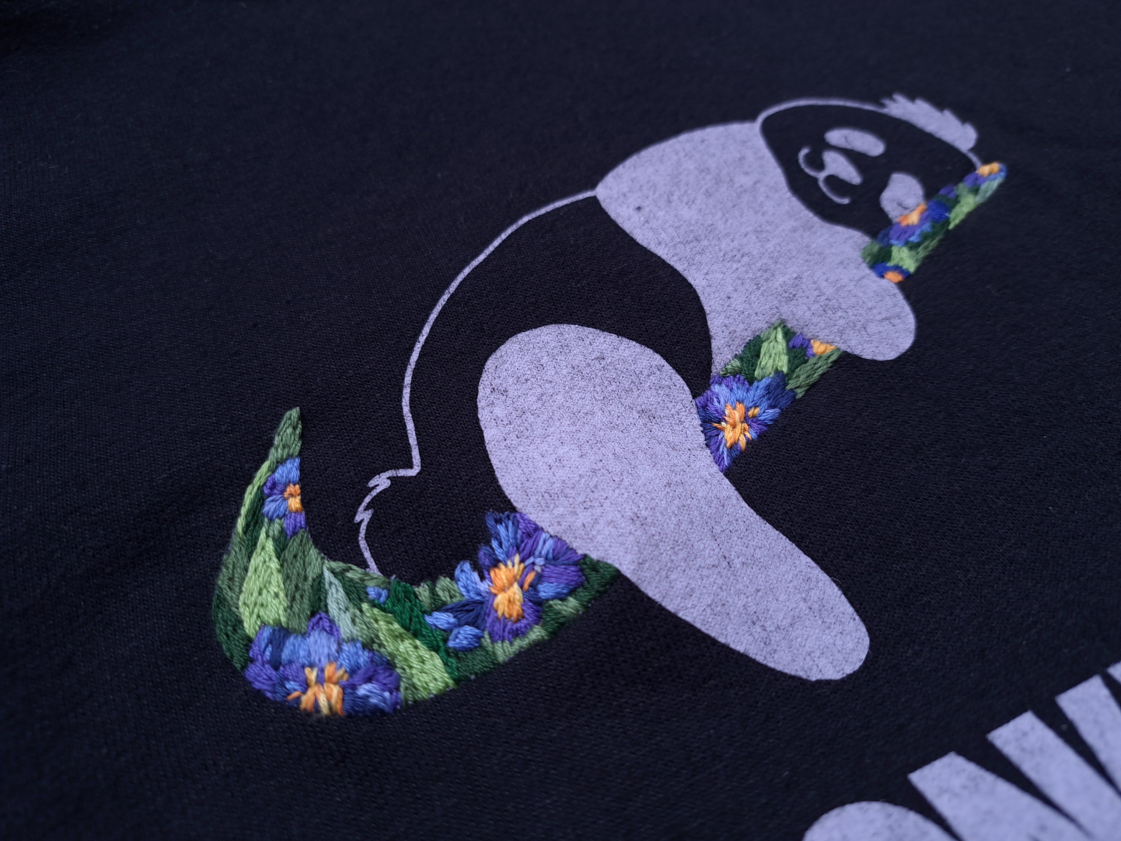 Close-up of thrifted sweatshirt featuring embroidered irises in Van Gogh style over a funny panda print, with deep blue petals, green leaves and lilac accents on cozy gray fabric 
